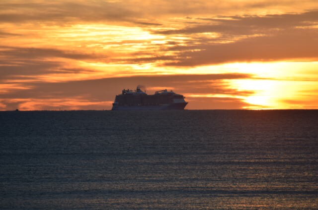 A profile of a cruise ship appears on the horizon as the rising sun creates a bright orange backdrop. 
