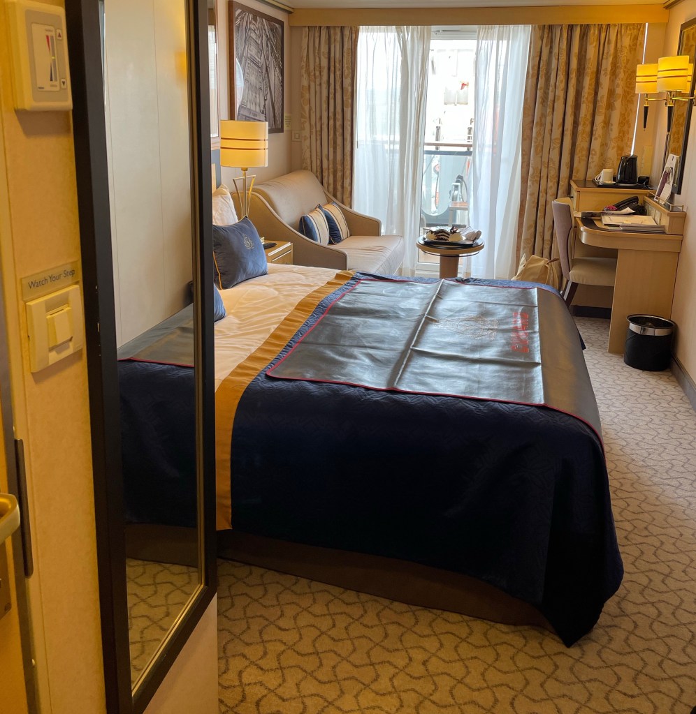 From a small hallway with a full length mirror, the cabin opens up to show a king size bed, followed by a sofa and table on one side and desk and chair on the other, and the exit to a private balcony. 