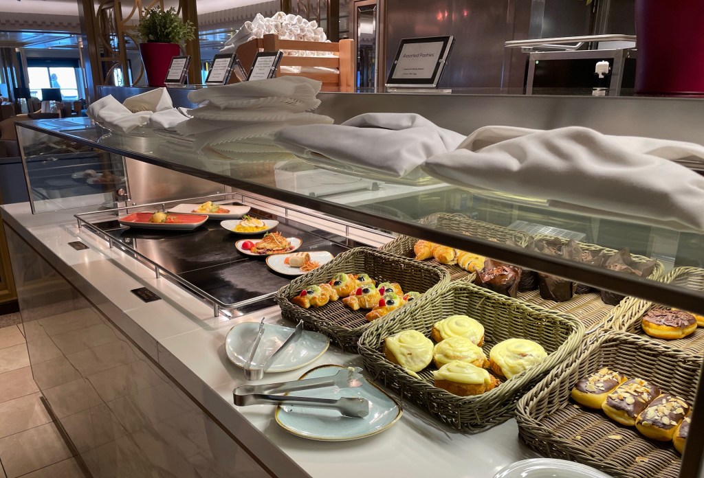 Buffet showing six plated breakfast meals and several baskets of large pastries. 