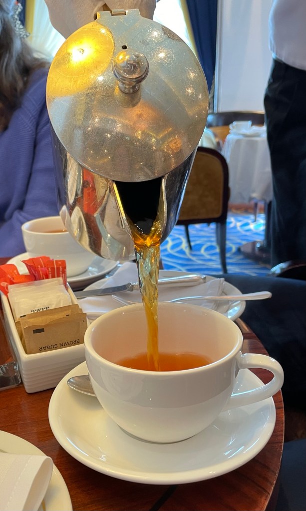Tea flows into a fancy tea cup from a silver teapot held by a waiter