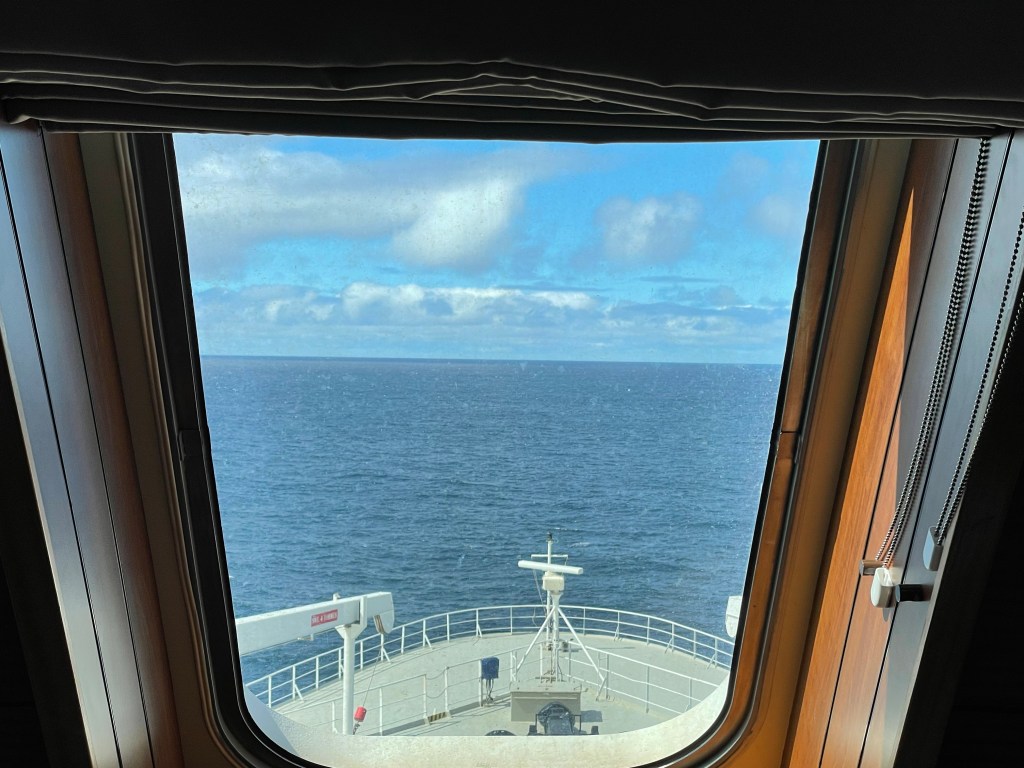 Expanse of ocean over ship bow, water is calm and daytime sky is partly cloudy 