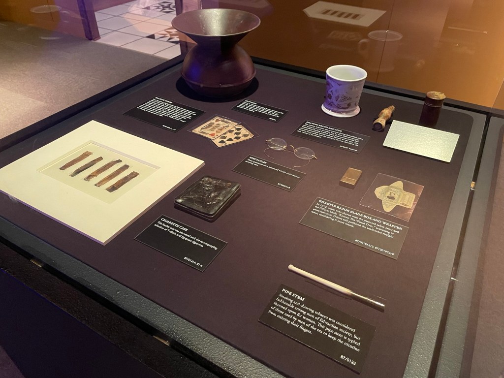 Info cards in the exhibit: shaving brush and mug the anthrax infection was of concern just as just as it is today but for different reasons. Unsterilized shaving brushes made from animal bristles like this one potentially carried anthrax bacteria which worked its way into the skin. Gillette razor blade box and wrapper in 1912 many men shaved with the patented safety razor and Gillette blade. Others preferred the traditional straight razor considering it more manly. Pipe stem typical of those used by men of the era to keep the nicotine from staining their fingers. Spectacles, recovered with their leather carrying case. Leather cigarette case recovered with a selection of Turkish and Egyptian cigarettes. The info cards for a spittoon and playing cards are too blurry to make out. 