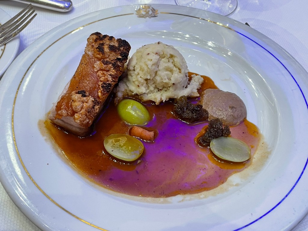 One on bone pork belly resembling a rib plus a scoop of potato and a few green grapes and raisins ass with a reddish brown sauce