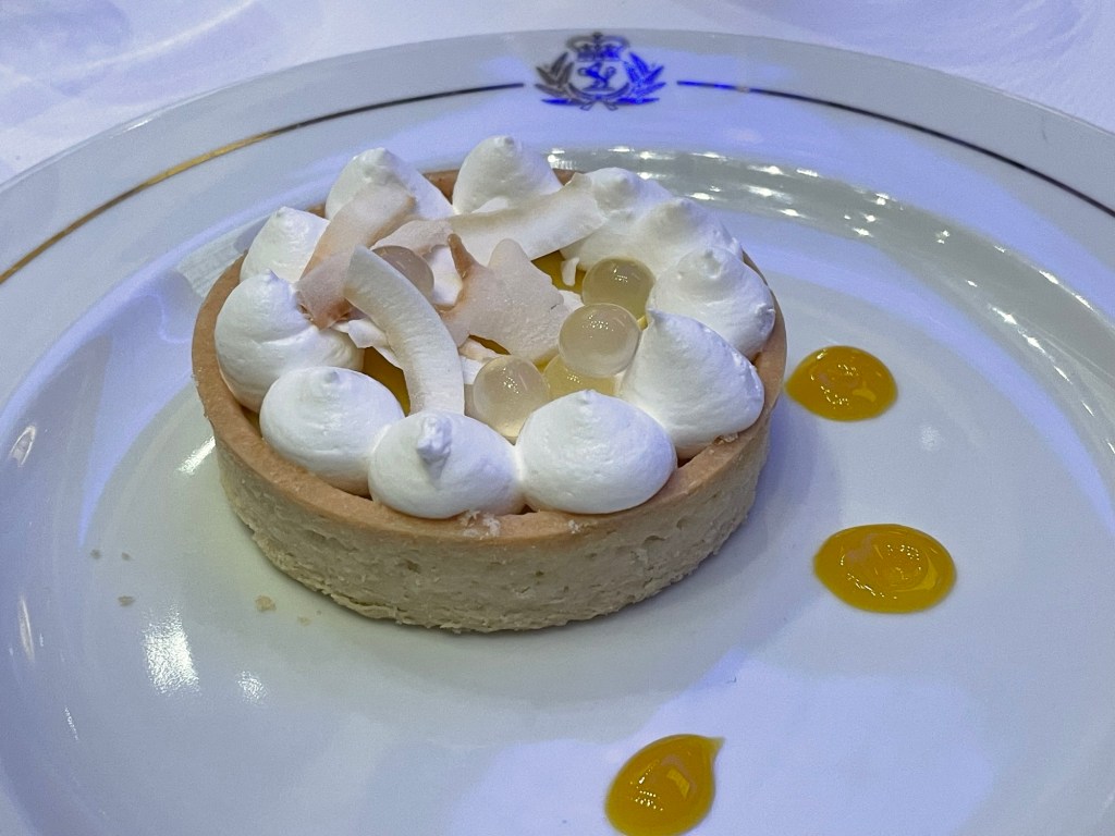Small round crust base filled with a fruit mousse and topped with 10 dollops of cream or meringue around the inner perimeter, several small orbs of passion fruit,  and shaved coconut on top. 