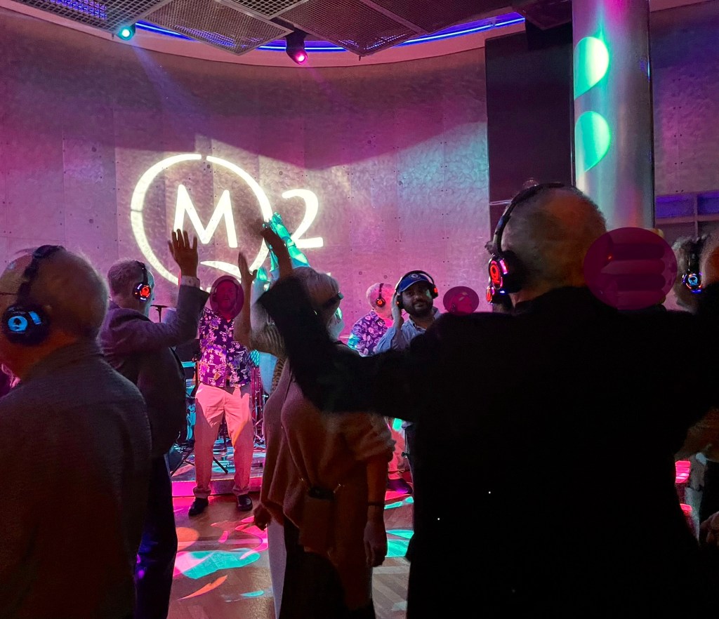 A somewhat crowded dance floor where everyone’s wearing headphones, some with blue lights and some with red lights