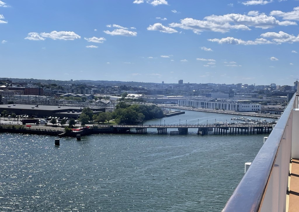 As viewed from the ships deck a narrow road crosses a channel, with the city taking shape in the background. 