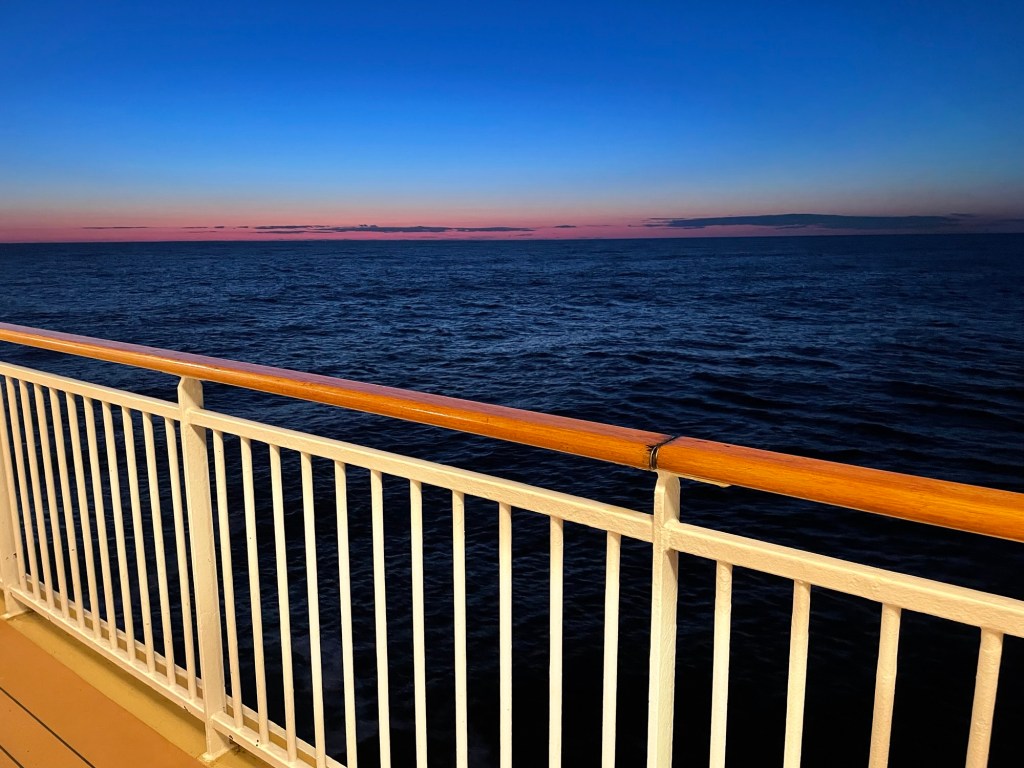 Ribbons of orange span the horizon between a calm dark blue ocean and deepening blue sky.
