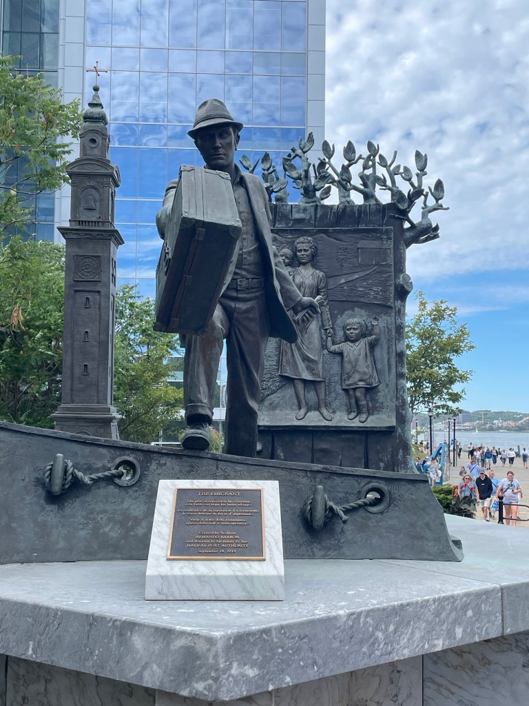  A bronze sculpture of an immigrant carrying a large trunk, with a woman and child behind him and a ship suggested in the relief. 